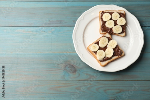 Toasts with chocolate paste and banana on light blue wooden table, top view. Space for text