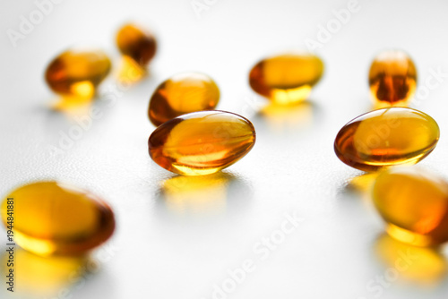 Close-up of amber softgel capsules on a white background with selective focus and clean lighting, ideal for healthcare and vitamin supplement concepts.