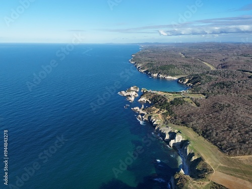 Scenic aerial view of a rugged coastal landscape featuring sea waves, rocky cliffs, clear blue water and untouched nature.