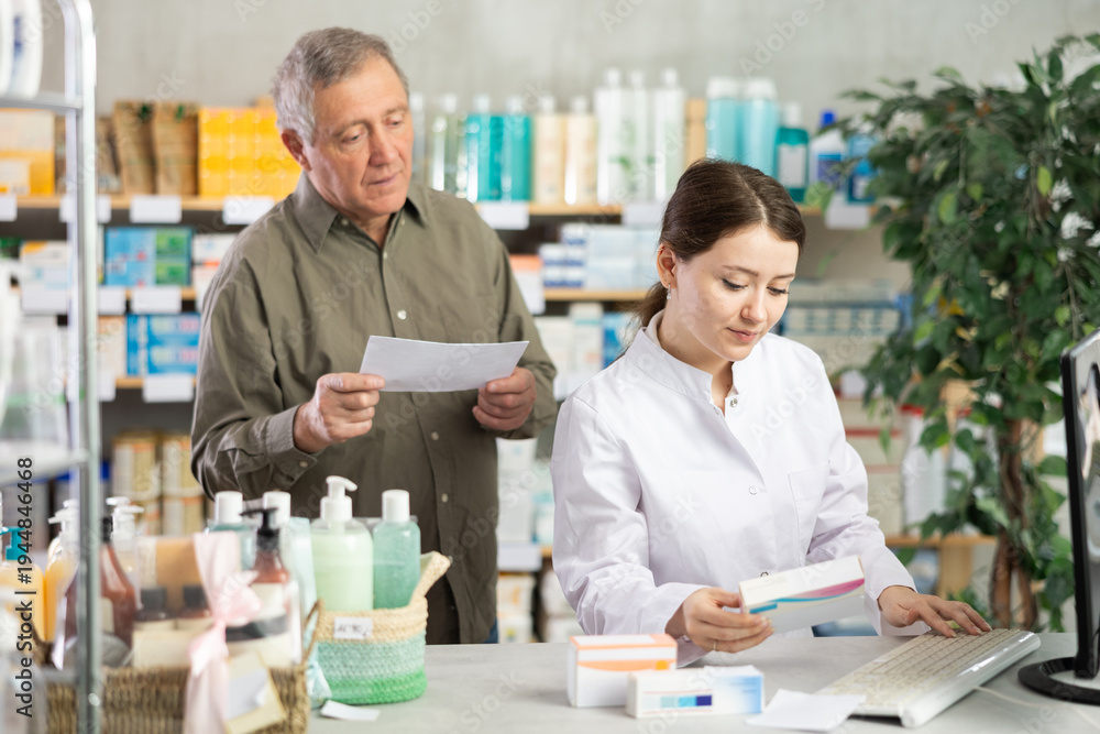 Obraz premium Woman employee at counter with computer sells pills and ointments to senior male customer upon request. Everyday life at pharmacy, consulting clients.