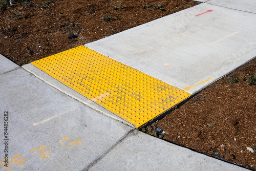 Foto Freshly installed concrete sidewalk, yellow ADA Curb Ramp, and landscaping in ne