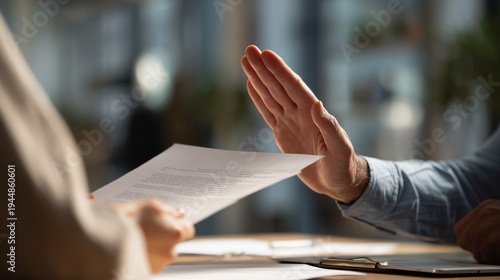 A business professional makes a definitive stop gesture, rejecting documents presented by a colleague during a serious discussion.