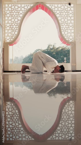 A Muslim man performing Islamic pray inside a mosque during Ramadan, a peaceful spiritual moment with beautiful mosque architecture and reflection on the polished floor.