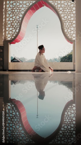 A Muslim man performing Islamic pray inside a mosque during Ramadan, a peaceful spiritual moment with beautiful mosque architecture and reflection on the polished floor.