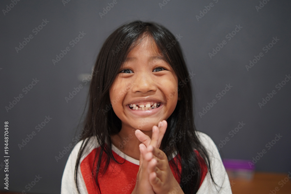 Fototapeta premium Cheerful little Asian girl clapping hands with a big smile, happy child celebrating success and feeling joyful, appreciation, achievement, and positive childhood emotion