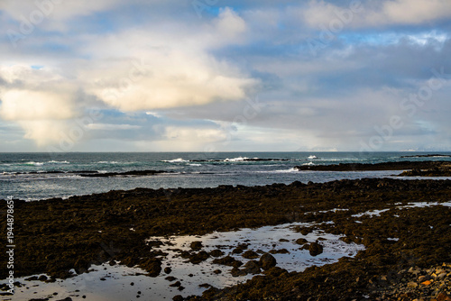 Dramatic coastal landscape with dark volcanic rocks, tide pools, and stormy clouds over the Atlantic ocean