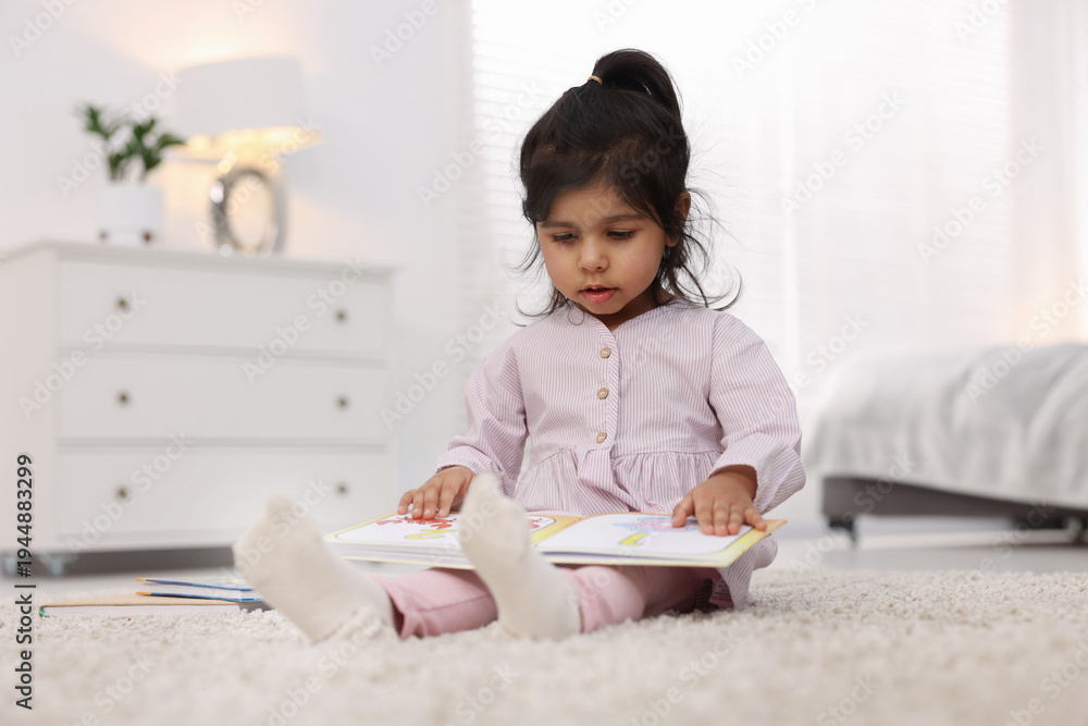 Naklejka premium Cute little girl reading book on floor at home. Space for text