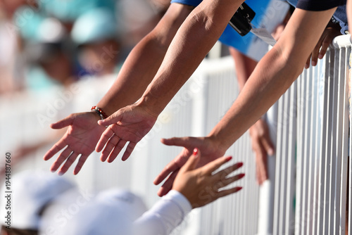 Athletes extend hands toward spectators at a sunny outdoor sports event, showing camaraderie and connection.