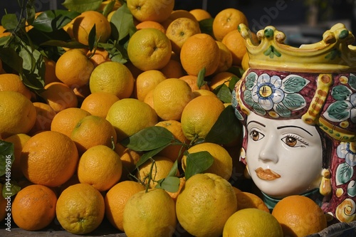 Local farmer's market fruit display stand with organic oranges decorated with a handmade ceramic Moorish head depicting a Sicilian woman in Marzamemi Sicily, Italy.