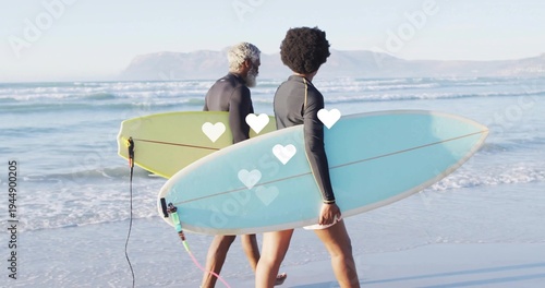 Φωτογραφία Walking two surfers toward ocean on beach, carrying surfboards with leashes, wea