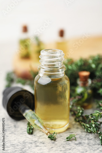 Bottles of thyme essential oil with fresh herbs and pipette on gray table, closeup