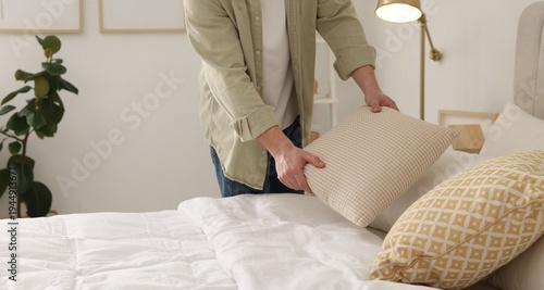 Fotografie Professional decorator arranging pillow onto bed indoors, closeup