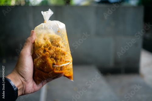 close up of hand holding take away Indonesia street food called batagor in transparent plastic package