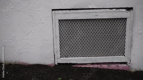Slow panning shot of a white exterior wall with a metal vent cover and textured stucco surface on the side of a building.