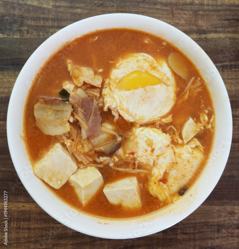 top view of gourmet Authentic Korean spicy soft tofu stew with egg, tofu cubes, seafood, and rich red chili broth served in a rustic bowl at Asian restaurant