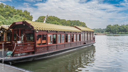 Beautiful Chinese boats are moored at the shore of the lake. Tiled roof, wood carvings, glass windows. Green vegetation, blue sky, clouds. China. Hangzhou. West Lake Xi Hu 