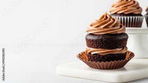 Two chocolate cupcakes with brown frosting on a white surface with a white background