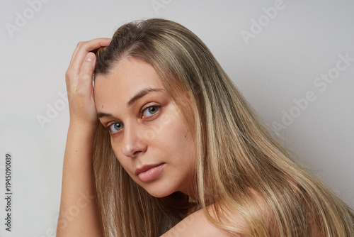 Natural portrait of a young woman with long hair in profile against a neutral background. Minimalist studio photo highlighting natural beauty, healthy skin, and authentic expression. 
