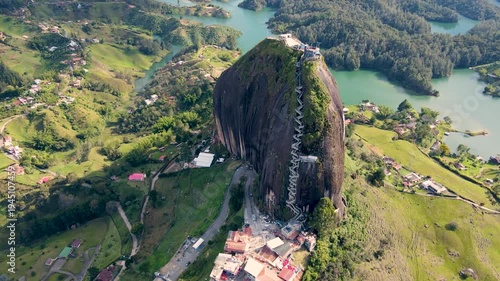 A stunning aerial shot captures the iconic El Peñol rock with lush green hills and the shimmering lake below in Guatapé, Colombia.