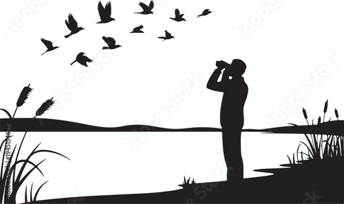 Man in silhouette looking through binoculars at flying birds by lake