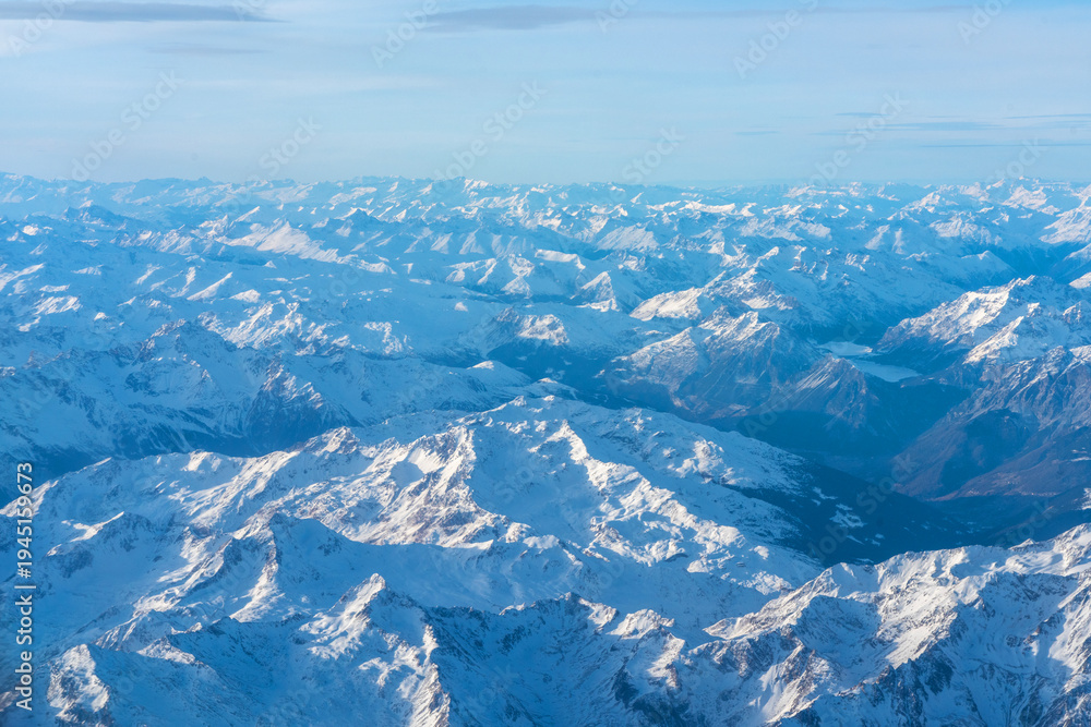 Fototapeta premium Plane view of mountains at sunrise, snow rock and blue cloudy sky aerial view