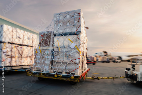 Cargo carts with freight in motion blur moving toward cargo airplane at airport. Air cargo logistics, airport ground operations, freight transport, and global trade concept.