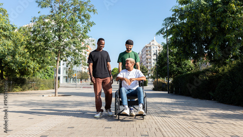 Young African American man in a wheelchair and his male friends walking together in the city. Panoramic image.