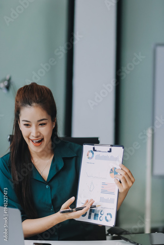 Determined asian businesswoman works late in a modern office, confidently analyzing data on her laptop, embodying success and professionalism with a smile