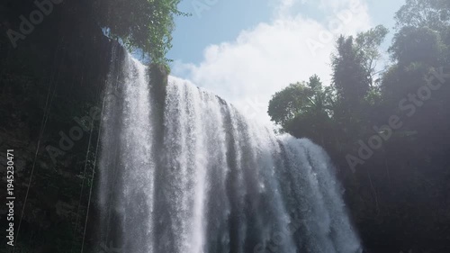 A majestic waterfall cascading down rocks with lush greenery and clear sky