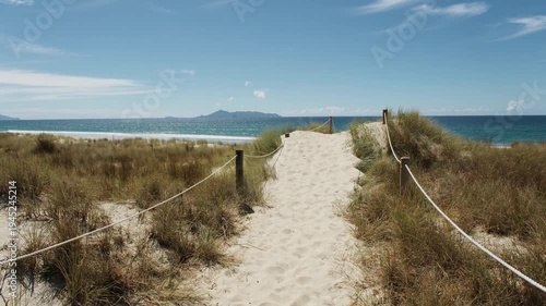 Sandy path through dunes leading to Mangawhai Beach with island view, New Zealand