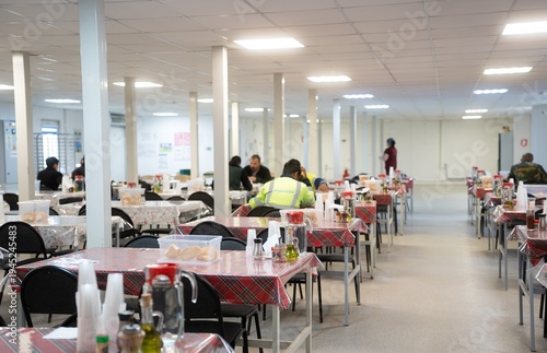 Industrial engineers sitting in canteen and talking on lunch break. Construction company workers in safety uniform eating meal and chatting in modern office