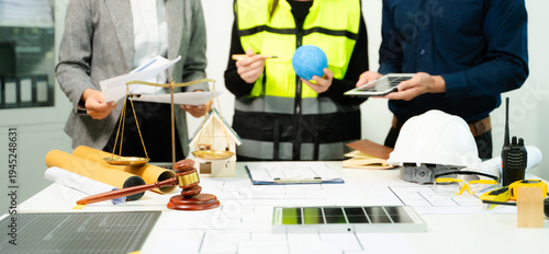 Legal and engineering professionals reviewing building plans with justice scale, gavel and safety equipment, symbolizing construction law, property regulation