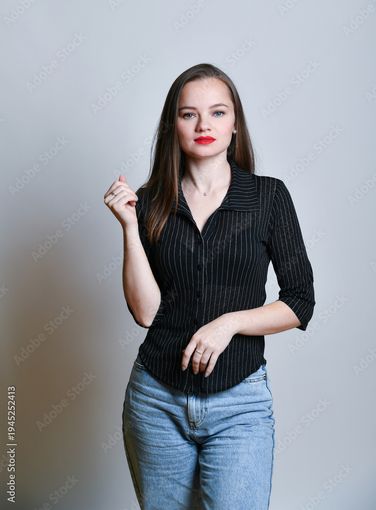 Naklejka premium Junge Frau in Jeans und schwarzer Bluse posiert selbstbewusst vor hellem Hintergrund. Modernes Fashion- und Lifestyleporträt mit Copyspace, Konzept für Stil, Mode und Persönlichkeit.