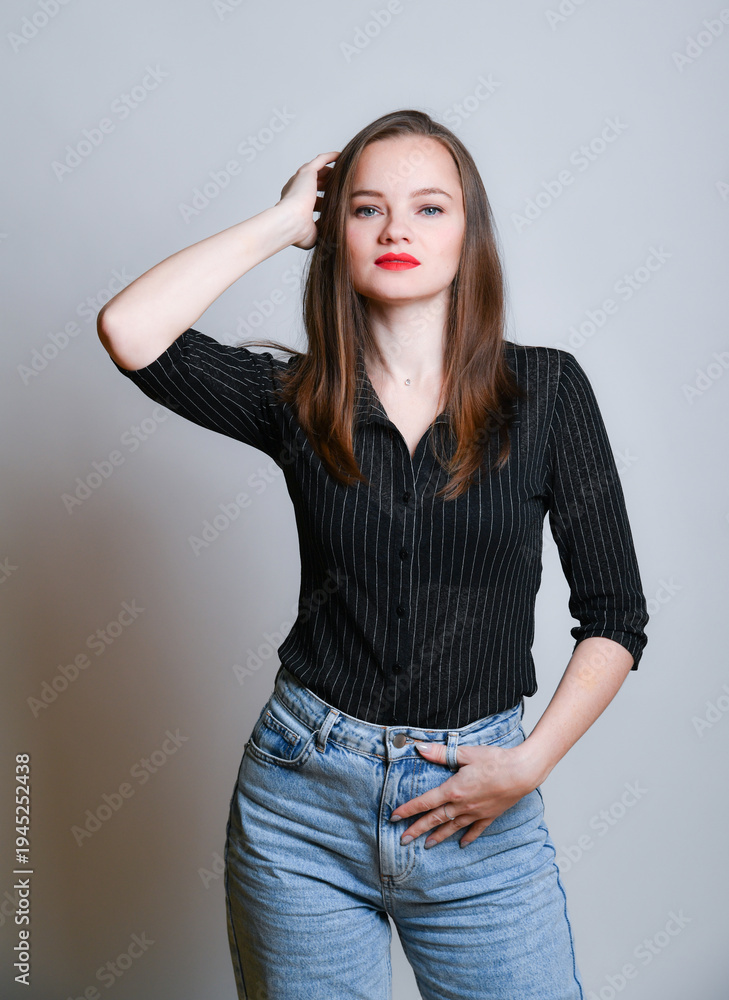 Obraz premium Junge Frau in Jeans und schwarzer Bluse posiert selbstbewusst vor hellem Hintergrund. Modernes Fashion- und Lifestyleporträt mit Copyspace, Konzept für Stil, Mode und Persönlichkeit.