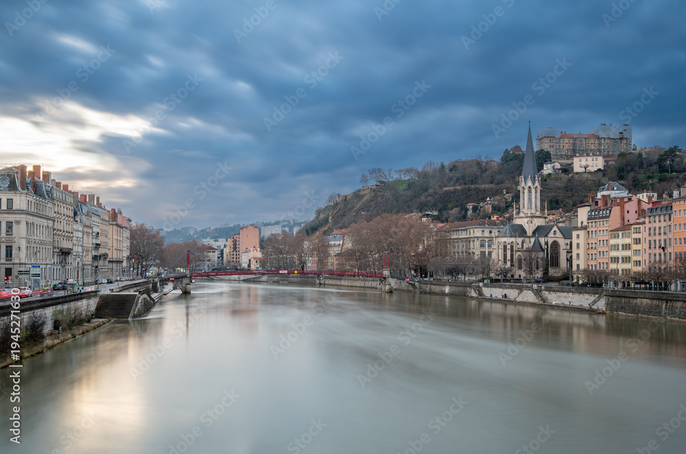 Fototapeta premium Lyon, france. December 29, 2023. Lyon cityscape showing the saône river, saint-georges church, and historic buildings under a cloudy sky during blue hour
