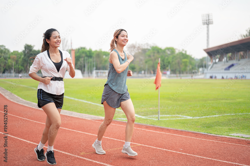 Obraz premium Full body of athletic asian woman and friend in sportswear running together on racetrack in stadium.