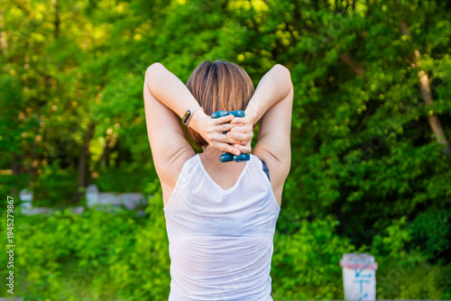 Foto Young Woman Doing Triceps Extension Exercises with Dumbbells in Sunny Green Park