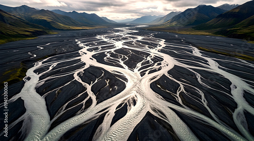 Aerial View of Braided River Delta with Silver Water Channels Splitting Across Dark Volcanic Gravel Plain with Distant Mountain Range Backdrop Overhead