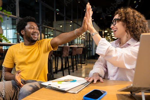 Disabled man in wheelchair and woman doing high five celebrating online collaboration
