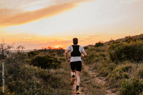 Cuadro en lienzo Trail runner running along a narrow mountain path toward a colorful sunset horizon
