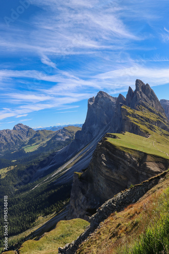 Panoramic view of Seceda ridge in the Dolomites, South Tyrol, Italy, showing dramatic jagged cliffs and lush alpine meadows under a clear summer sky
