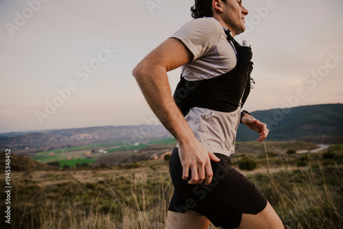Side profile of a male trail runner moving dynamically across rugged natural terrain during an endurance training run.