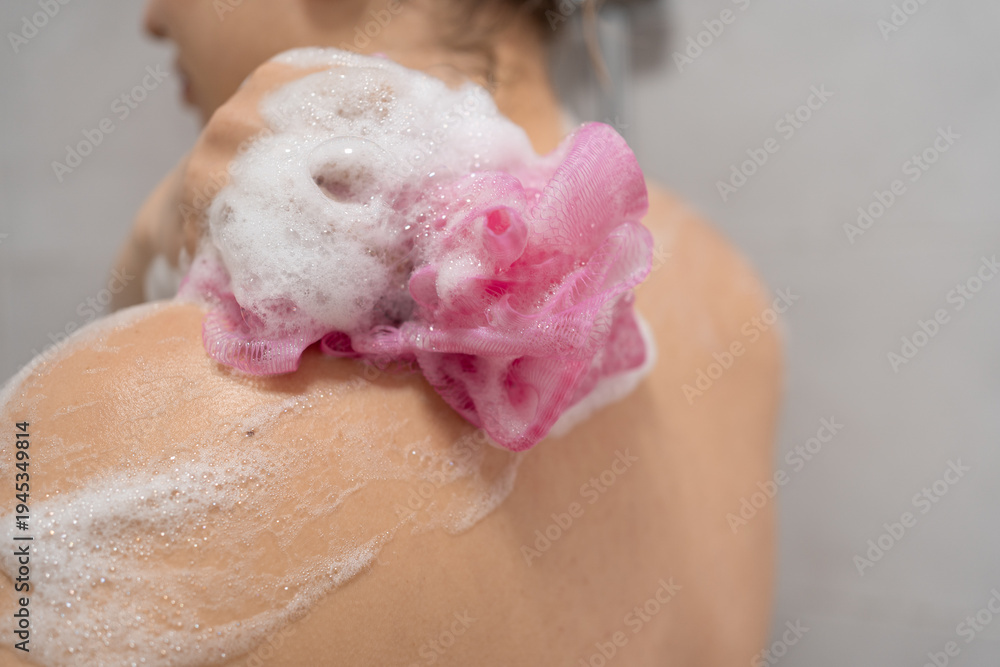 Fototapeta premium Close up of woman back washing with sponge and shower gel foam. Female scrubbing skin in bathroom. hygiene, body care, skincare and wellness routine in shower.