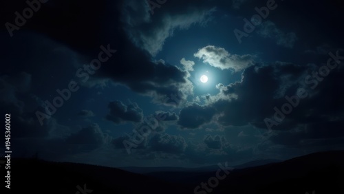 Nightscape with glowing full moon peeking through dramatic clouds over a dark, hilly horizon