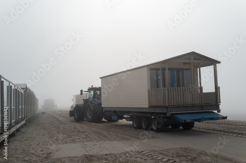 Quadro su tela Tractor transporting temporary beach house during foggy weather