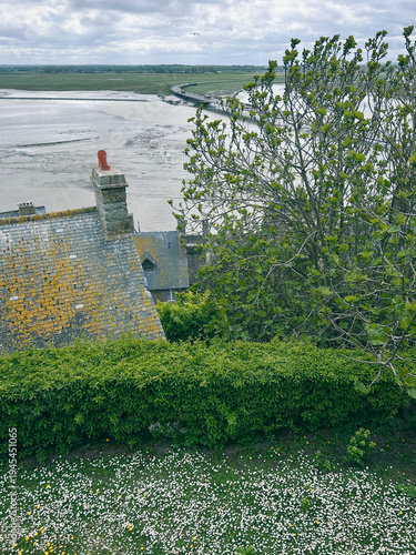 View from the Mont-Saint-Michel Abbey walls over the rooftops of the old buildings, new bridge and the English Channel at low tide on a windy spring day.