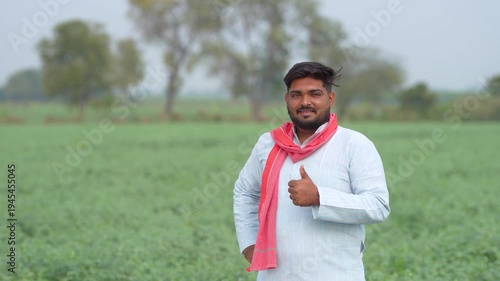 young indian farmer standing at green agricultural field