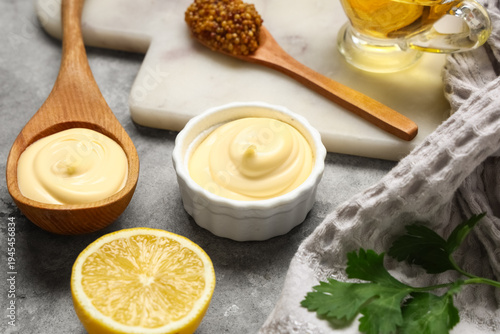 Foto Homemade mayonnaise in bowl and wooden spoon with lemon, mustard and oil on gray