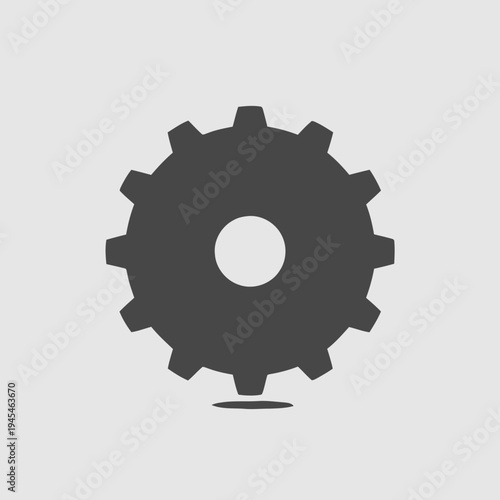 A dark gray, minimalist, vector icon of a cogwheel or gear, representing mechanics and industry, isolated on a light gray background with a subtle shadow