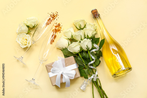 Beautiful white rose flowers with gift box, glasses and bottle of champagne on beige background